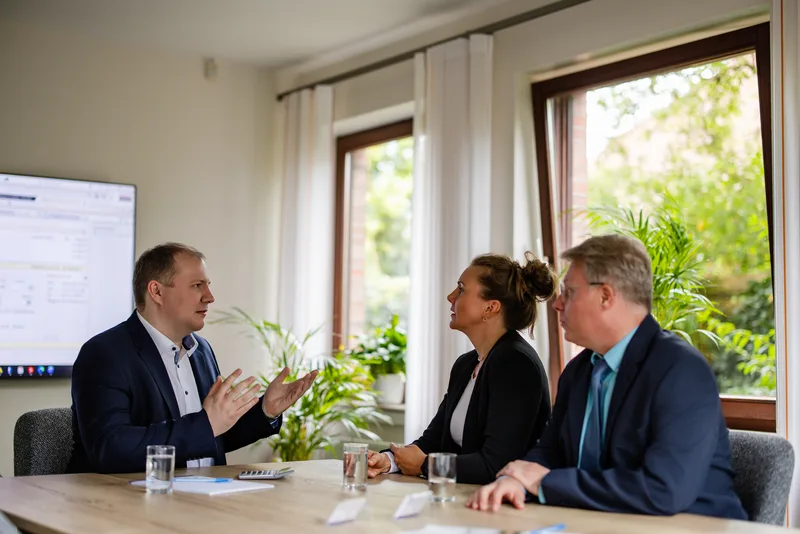 Steuerberater der Kanzlei RKK erklärt zwei Personen am Besprechungstisch engagiert ein Thema