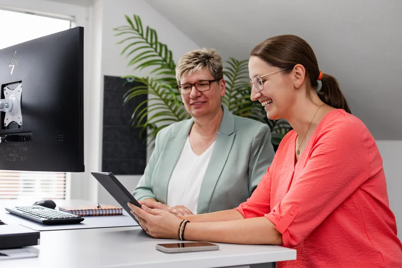Zwei Mitarbeiterinnen der Kanzlei RKK schauen gemeinsam auf ein Tablet am Schreibtisch
